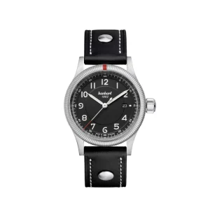 Reloj de piloto Hanhart Pioneer con bisel estriado, marcador rojo a las 12, esfera negra con números arábigos y correa de piel negra con remaches metálicos.